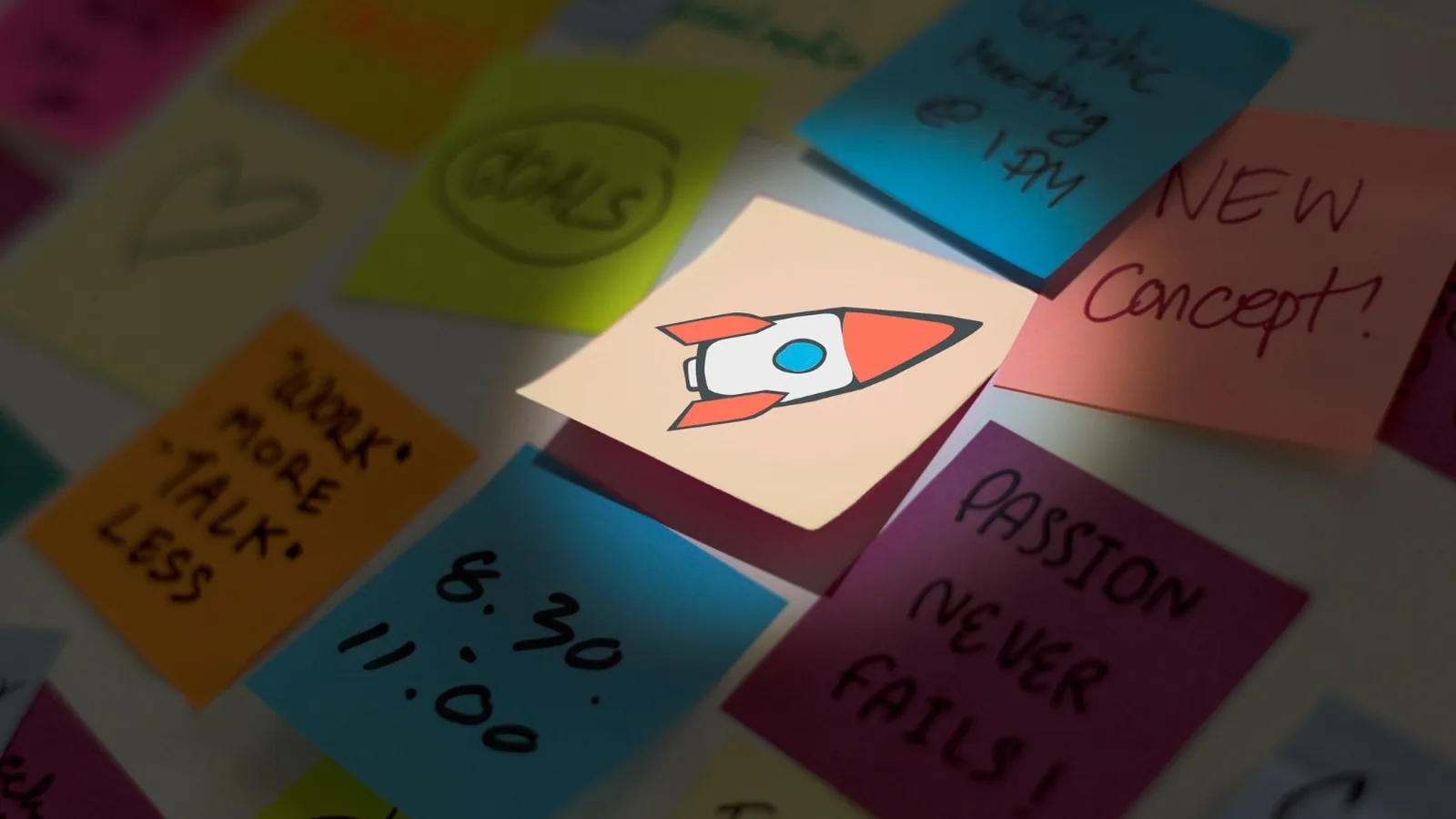 A spotlit sticky note with a rocket drawing standing out among other handwritten notes on a board